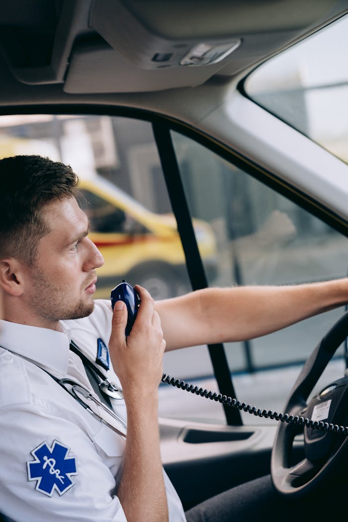 Professional paramedic in uniform using radio in ambulance while driving to emergency location.